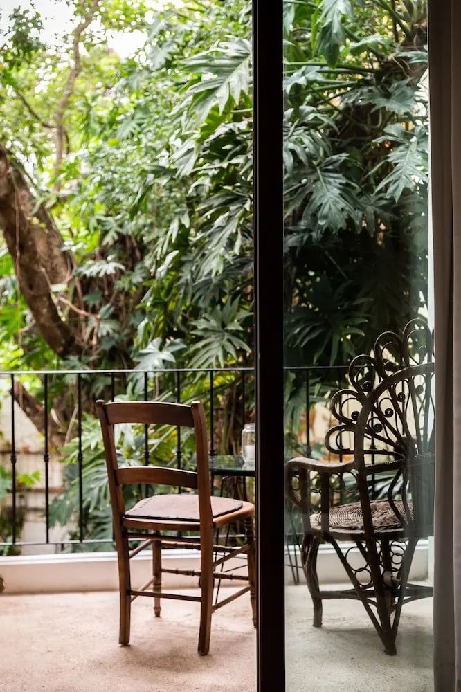 Blick durch eine Glastür auf einen Balkon mit Stühlen und grünen tropischen Pflanzen.