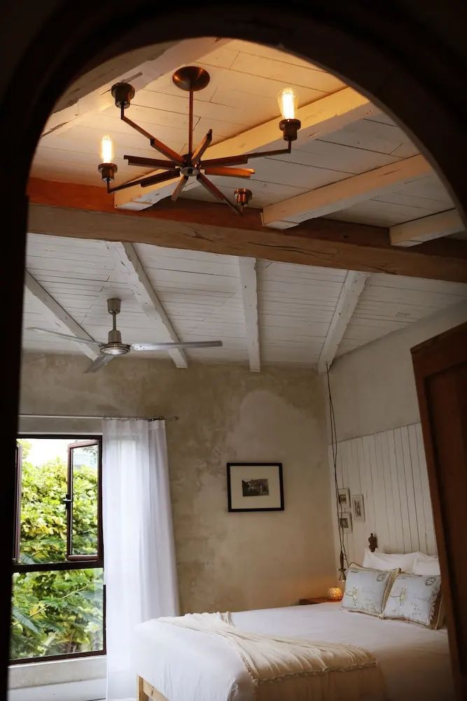 Blick auf die weiße Holzbalkendecke mit einem Deckenventilator und einer Holzlampe im Zimmer.
