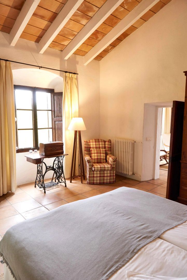 Rustikales Hotelzimmer mit Holzbalkendecke, Sessel, Nähmaschinentisch und Fenster.