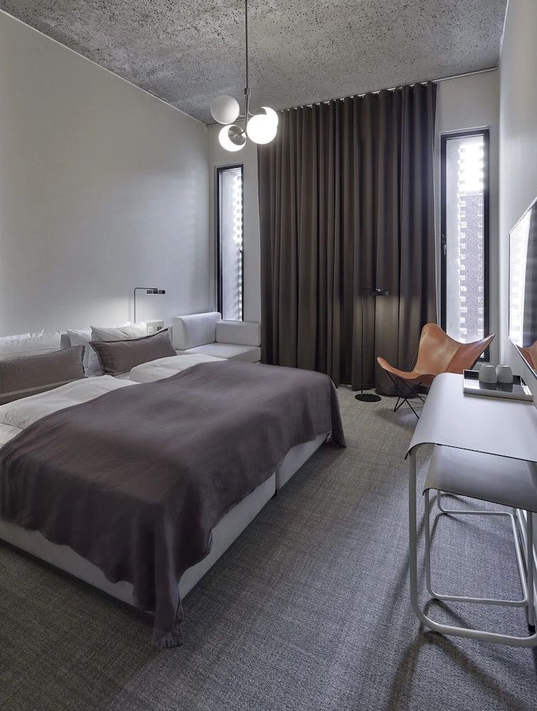 Modernes Hotelzimmer mit Doppelbett, Lederstuhl und dunklen Vorhängen.