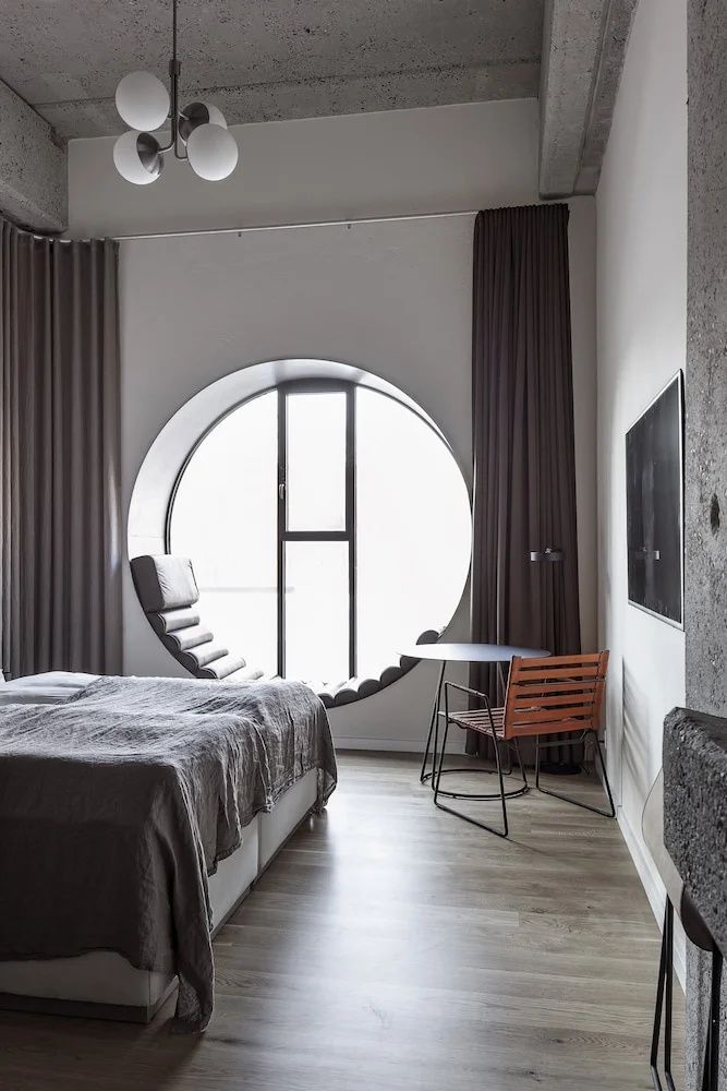 Doppelzimmer mit rundem Fenster, integrierter Sitznische und Stuhl am kleinen Tisch.