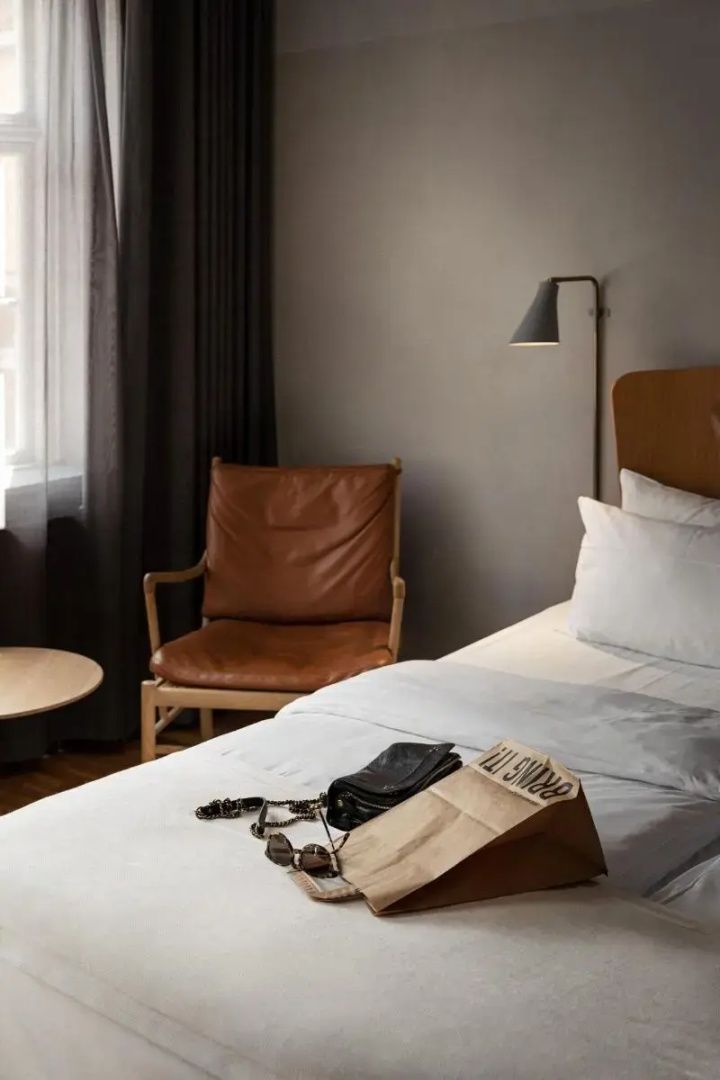 Ein Bett mit weißer Bettwäsche neben einem Ledersessel in einem modern eingerichteten Hotelzimmer.
