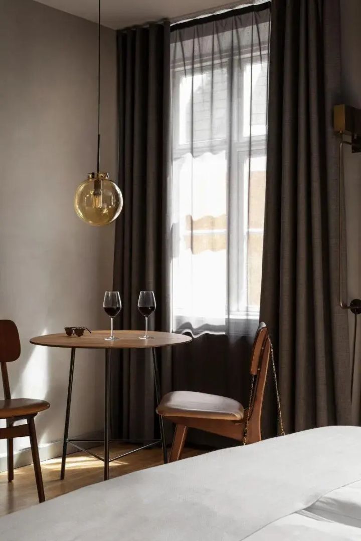 Sitzbereich im Hotelzimmer mit Holztisch, Stühlen und zwei Gläsern Rotwein.