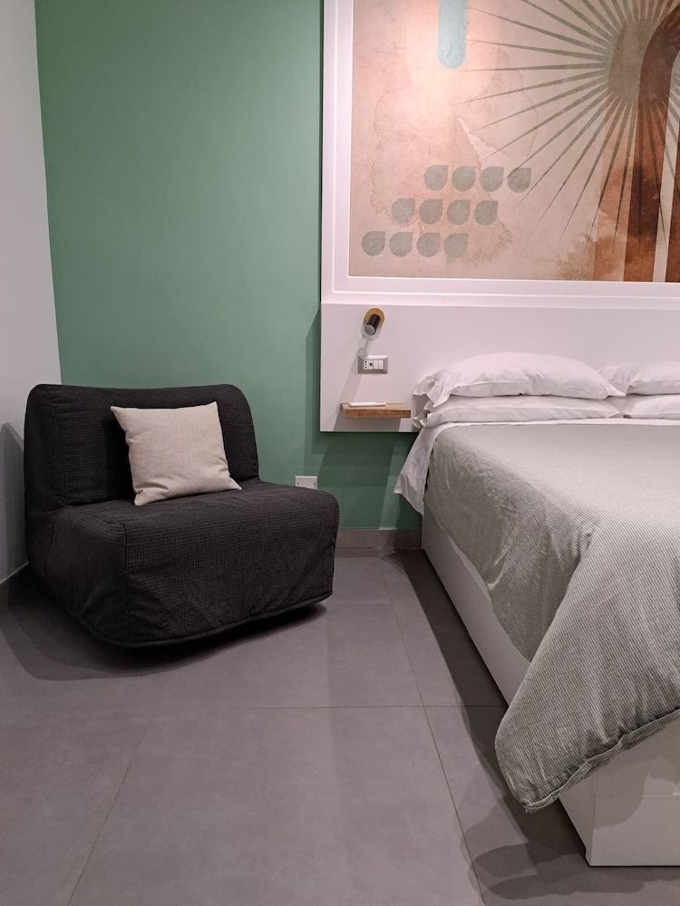 Dunkler Sessel mit Kissen neben einem Bett mit weißer Bettwäsche.