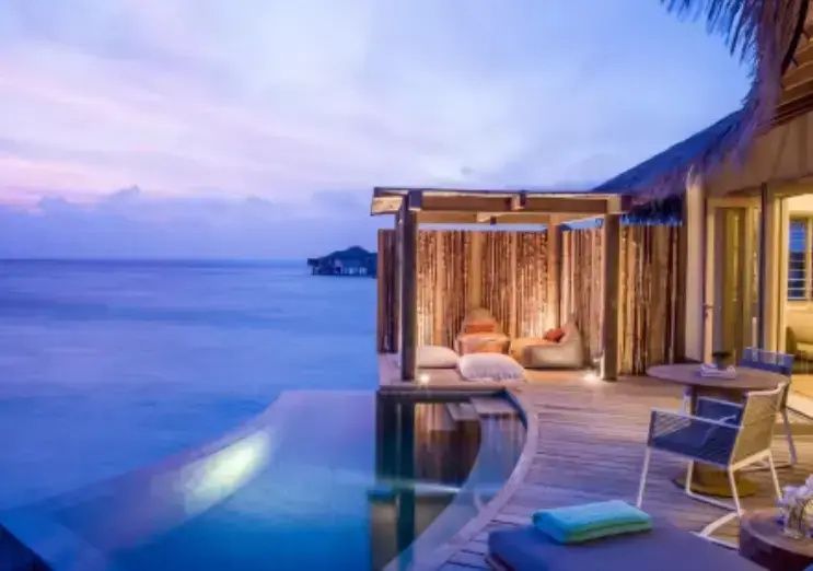 Holzterrasse einer Villa mit Privatpool, Loungebereich und freiem Blick auf das Meer bei Dämmerung.