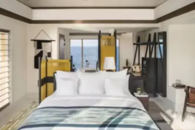Schlafzimmer mit großem Doppelbett, weißen Kissen und Blick auf das blaue Meer.