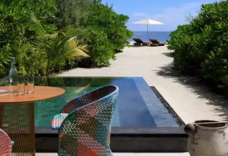 Terrasse einer Villa mit kleinem Pool, buntem Stuhl und Blick auf den Strand.