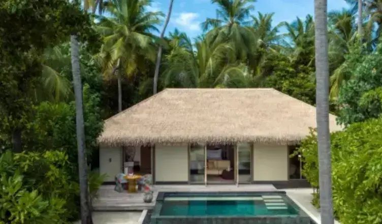 Außenansicht einer Villa mit Reetdach, Holzterrasse und eigenem Pool inmitten von Palmen.