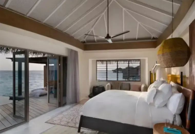Schlafzimmer einer Overwater-Villa mit großem Doppelbett, hohen Decken und Blick aufs Meer.