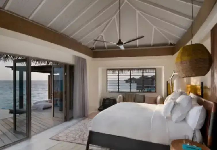 Schlafzimmer einer Überwasservilla mit großem Doppelbett und Blick auf das Meer.