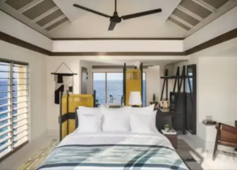 Hell eingerichtetes Schlafzimmer mit Doppelbett, Deckenventilator und Meerblick.