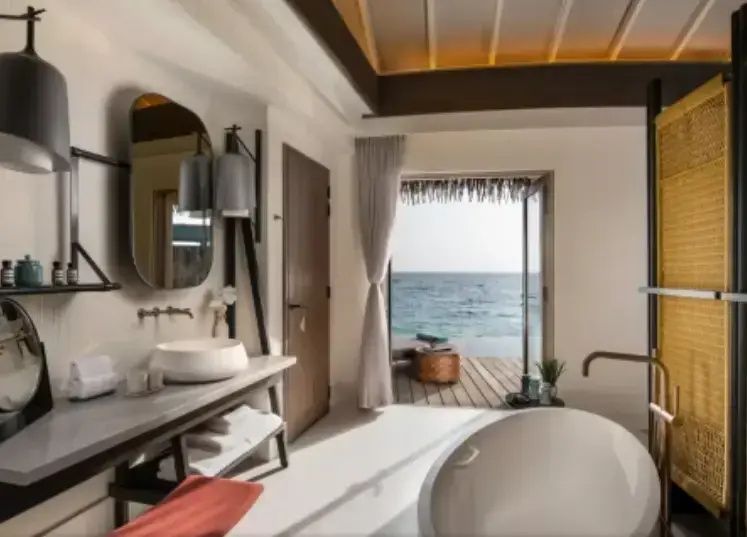 Badezimmer einer Wasser-Villa mit freistehender Badewanne, Waschtisch und Meerblick.