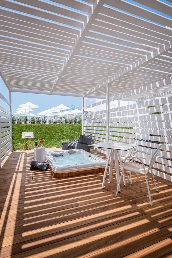 Überdachte Holzterrasse mit Whirlpool, gemütlicher Sitzgelegenheit und Sonnenschutz.