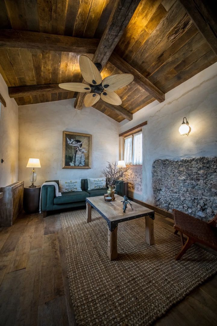 Wohnbereich mit grünem Sofa, Holztisch, Deckenventilator und Natursteinwand