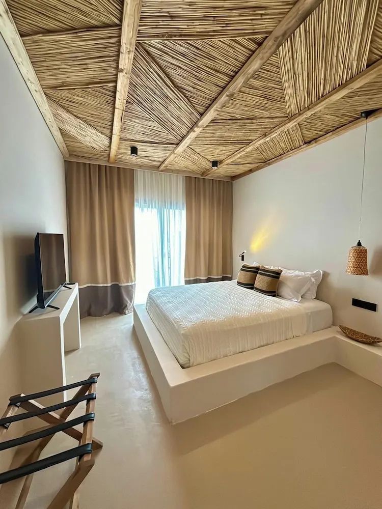 Modernes Hotelzimmer mit Doppelbett, Flachbild-TV und einer Decke aus Schilfrohr.