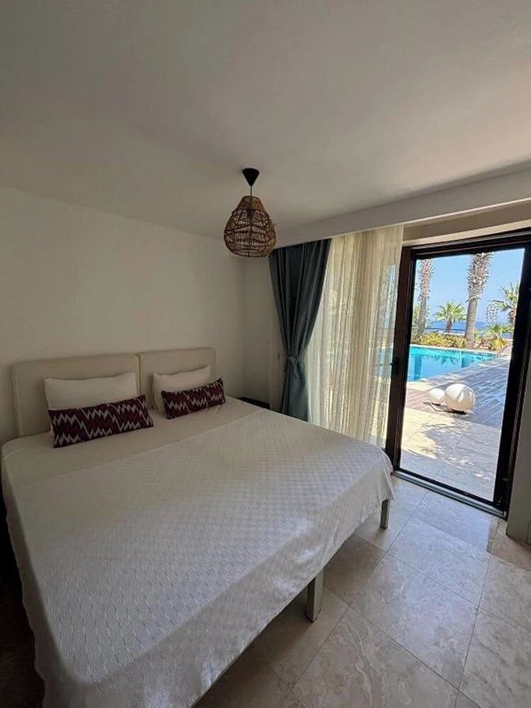 Hotelzimmer mit Doppelbett, Kissen und Blick durch die Glasschiebetür auf den Pool.