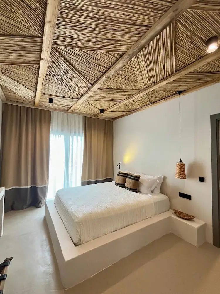 Hell eingerichtetes Schlafzimmer mit beigen Vorhängen und weißem Doppelbett.