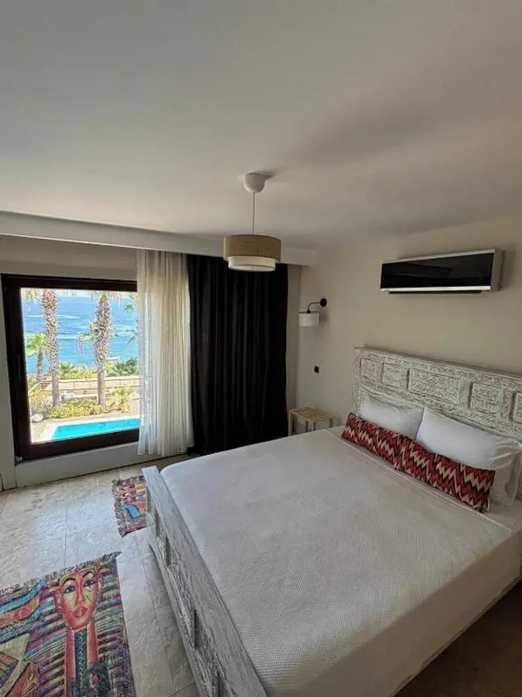 Schlafzimmer mit Doppelbett, hellem Kopfteil und Ausblick auf Pool und Meer.