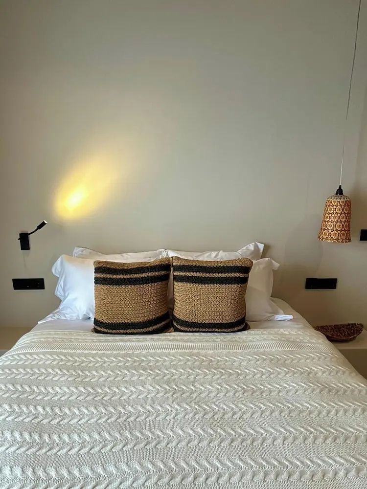 Doppelbett mit weißer Strickdecke, Kissen, Wandleuchte und einer hängenden Lampe.