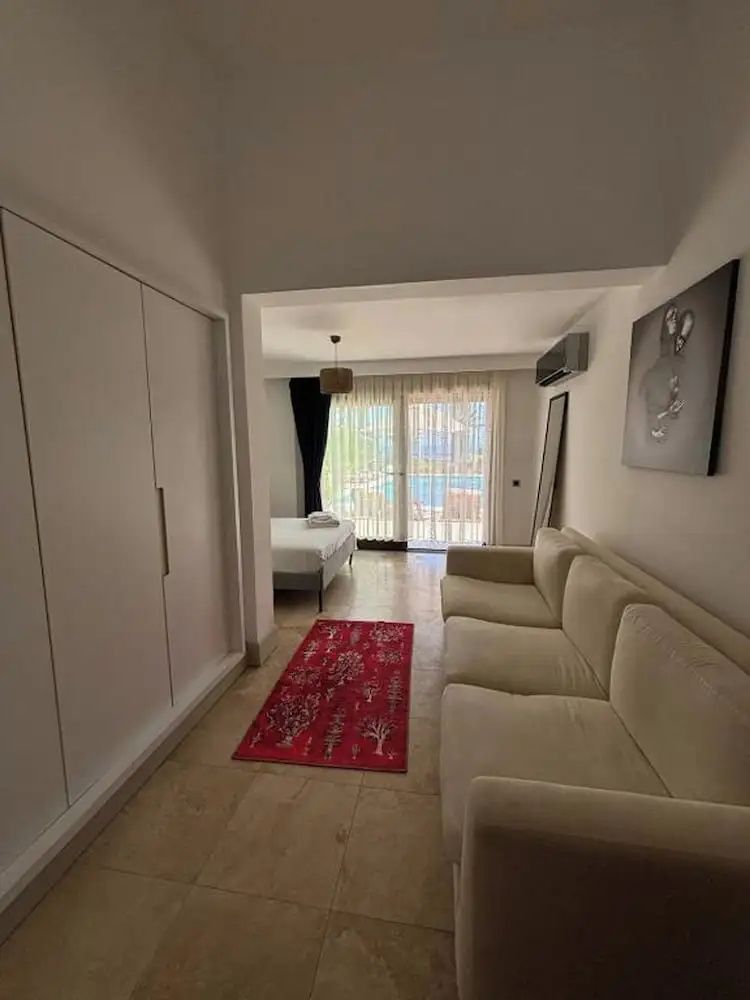Wohnbereich einer Suite mit hellem Sofa, rotem Läufer und Blick zum Schlafbereich.