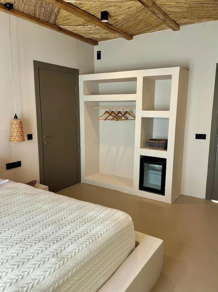 Offener weißer Einbauschrank mit Minibar und Kleiderbügeln neben einem Doppelbett.