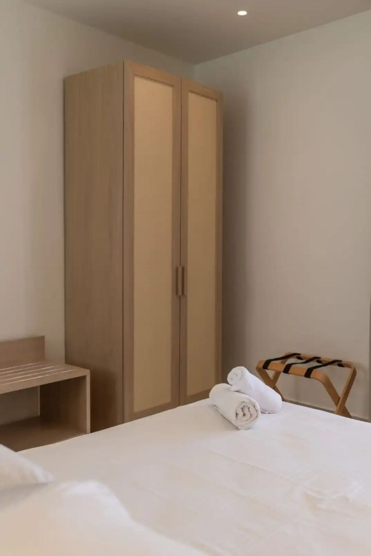 Ausschnitt eines Schlafzimmers mit einem Kleiderschrank aus Holz, Gepäckablage und Bett.