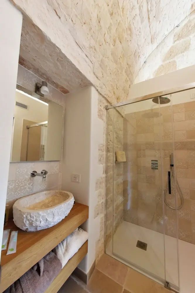 Badezimmer mit einem Waschtisch aus Stein, Spiegel und ebenerdiger Glasdusche.