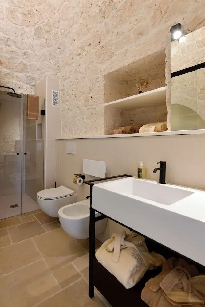 Modernes Badezimmer mit Steinwänden, Glasdusche, weißem Waschbecken und Toilette.