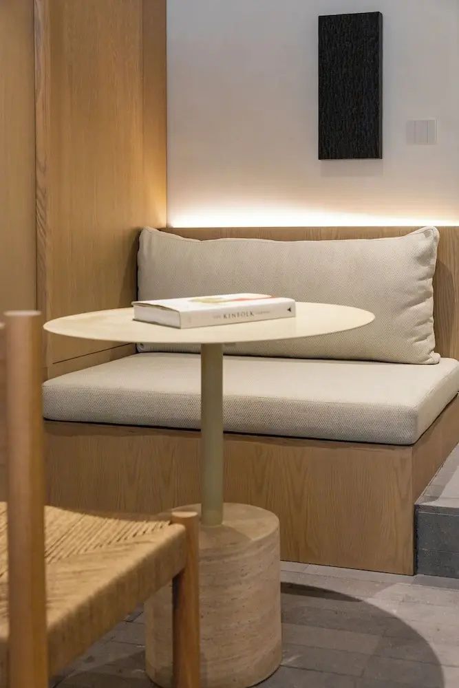 Sitzecke im Hotelzimmer mit beige gepolsterter Bank und einem kleinen runden Beistelltisch.