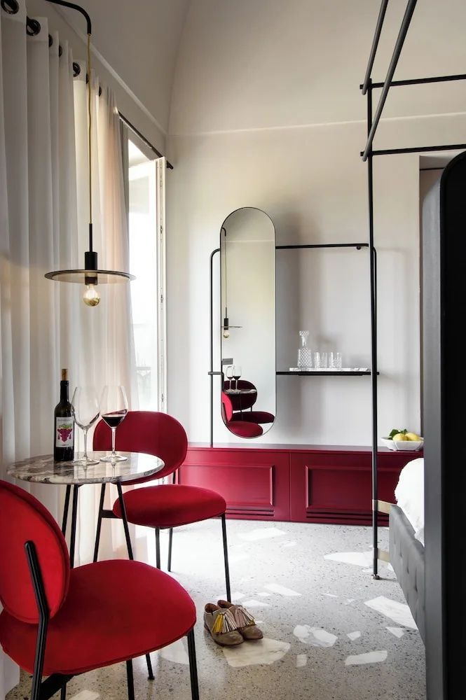 Sitzecke im Hotelzimmer mit zwei roten Sesseln, Marmortisch und einem ovalen Spiegel.