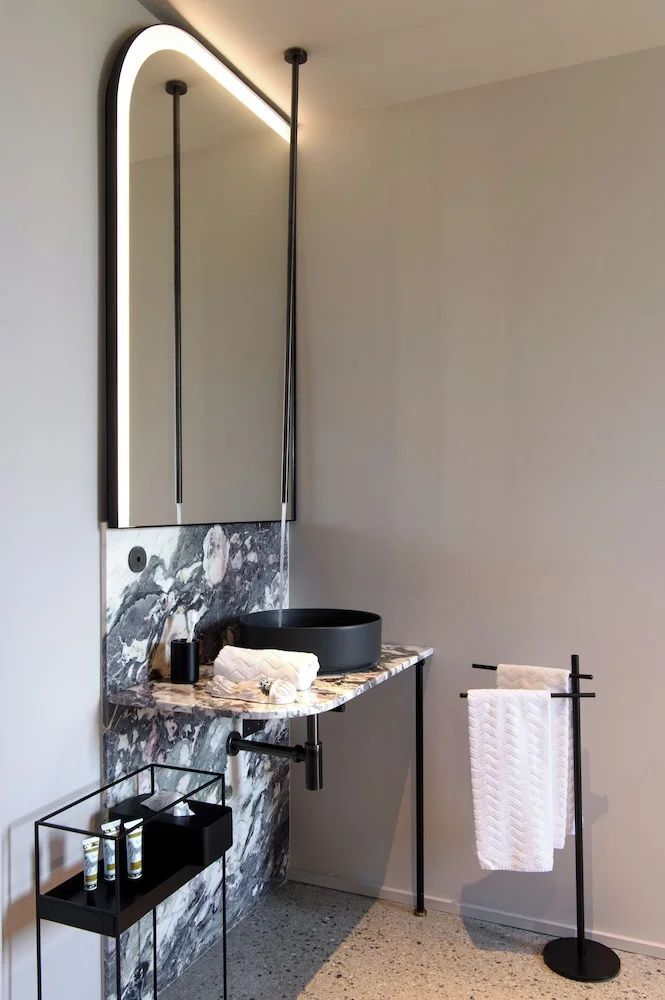 Modernes Badezimmer mit schwarzem Aufsatzwaschbecken, Marmordetails und hohem Spiegel.