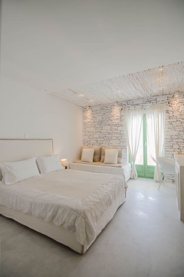Helles Hotelzimmer mit Doppelbett, Natursteinwand und weißen Möbeln.