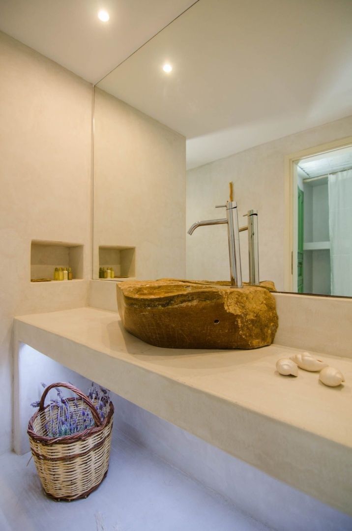 Waschbecken aus Naturstein auf einer hellen Ablage mit großem Spiegel im Badezimmer.
