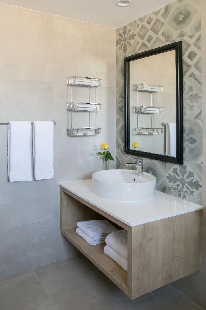 Badezimmer mit Waschtisch, rundem Waschbecken, rechteckigem Spiegel und Wandfliesen.