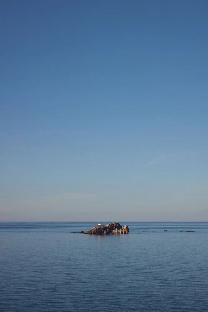 Ruhiges blaues Meer mit einer kleinen Felseninsel in der Ferne unter einem klaren Himmel.