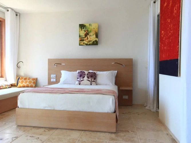 Helles Hotelzimmer mit einem Doppelbett, Kopfteil aus Holz und weißer Bettwäsche.