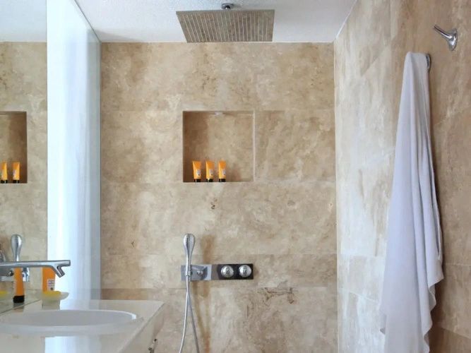 Dusche mit großer Regendusche, hellen Fliesen aus Naturstein und einer Nische in der Wand.