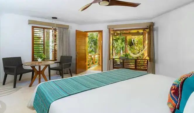 Blick durch das Schlafzimmer mit geöffneter Tür auf tropische Pflanzen und eine Hängematte.