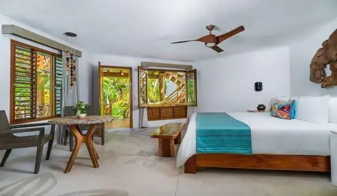 Großzügiges Hotelzimmer mit Doppelbett, Sitzbereich und Blick ins Grüne durch offene Türen.