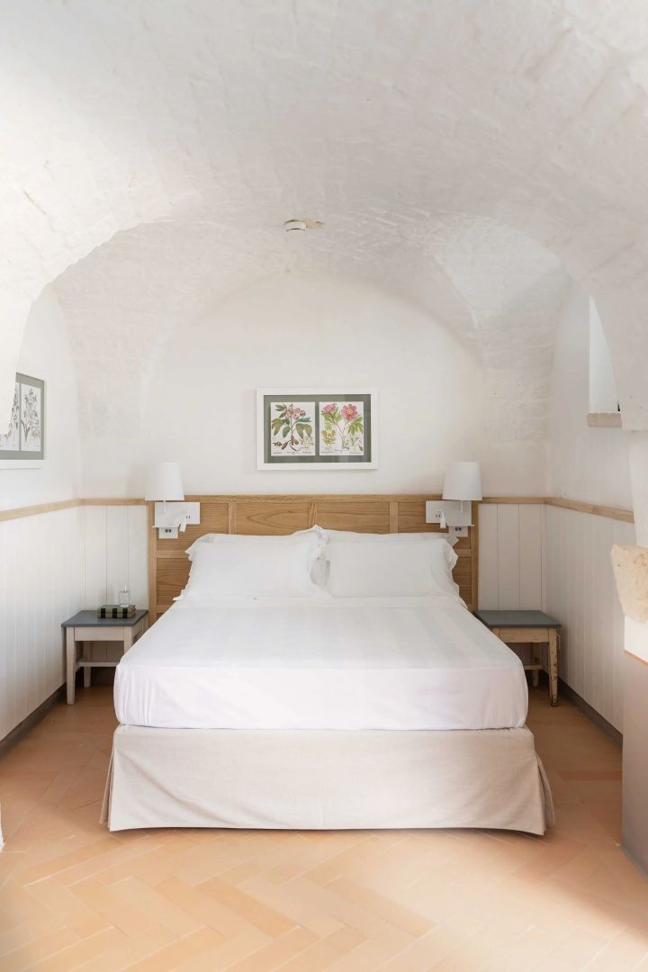 Schlafzimmer mit Tonnengewölbe, weiß bezogenem Doppelbett und Holzkopfteil.