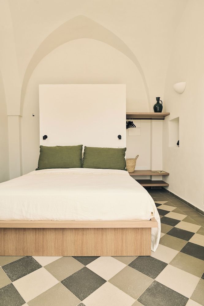 Doppelbett mit grünen Kissen vor einer weißen Wand und Fliesenboden.