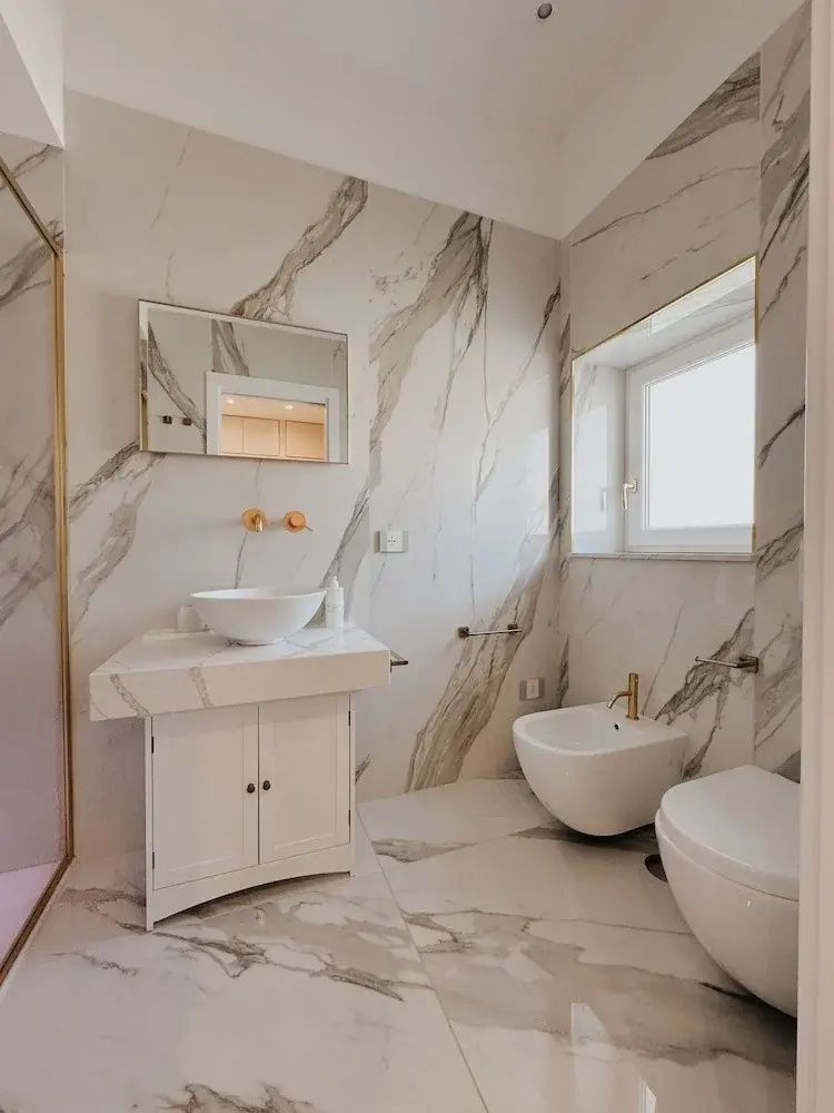 Hell gefliestes Badezimmer mit Marmormuster, Waschbecken auf Unterschrank, Bidet und WC.