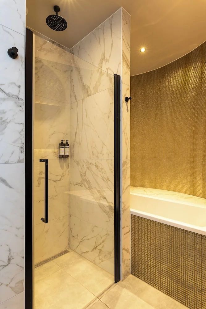Badezimmer mit einer Dusche samt Glastür und einer Badewanne mit goldener Mosaikwand.