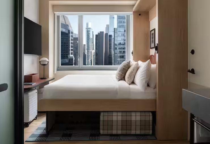 Doppelbett in einem modernen Hotelzimmer vor einem Fenster mit Blick auf Hochhäuser