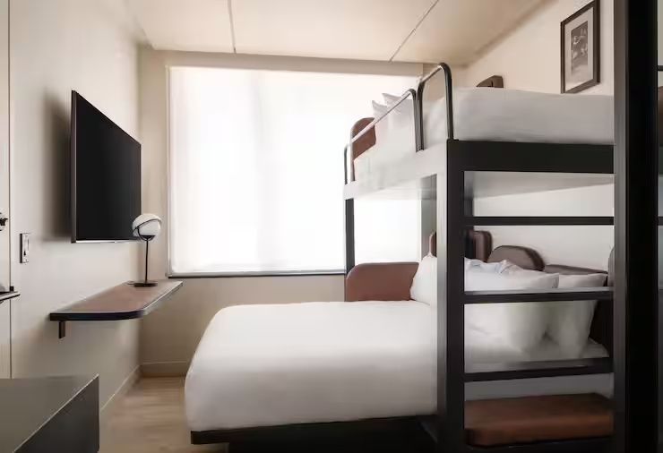 Modernes Hotelzimmer mit einem Etagenbett, weißer Bettwäsche und Wandfernseher.