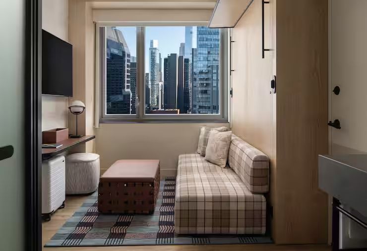 Sitzbereich im Hotelzimmer mit kariertem Sofa und Fensterfront zu Wolkenkratzern