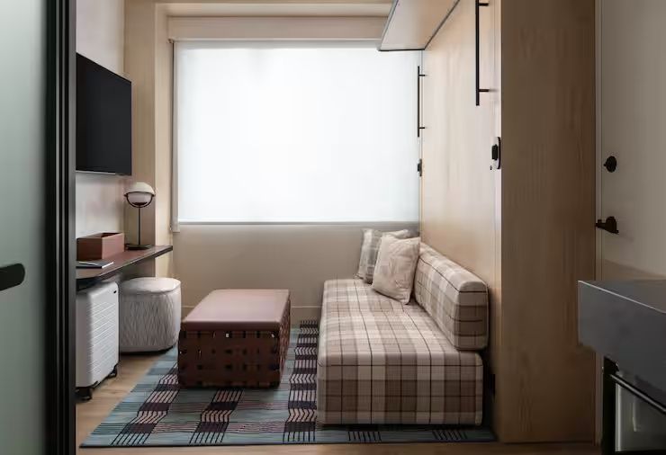 Sitzbereich im Hotelzimmer mit kariertem Sofabett und niedrigem Tisch vor dem Fenster.