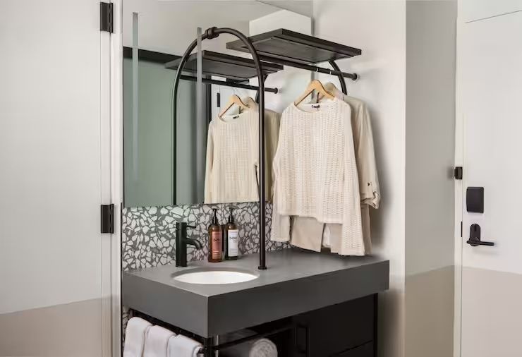 Moderner Waschplatz im Badezimmer mit grauer Arbeitsplatte, Spiegel und Kleiderstange.