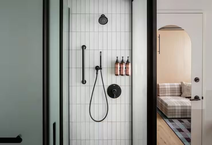 Weiße geflieste Dusche mit schwarzer Armatur und montierten Spenderflaschen