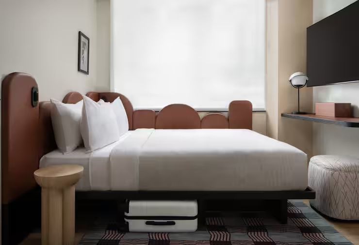 Modernes Hotelzimmer mit einem Doppelbett, weißer Bettwäsche und Kofferstaufach darunter.